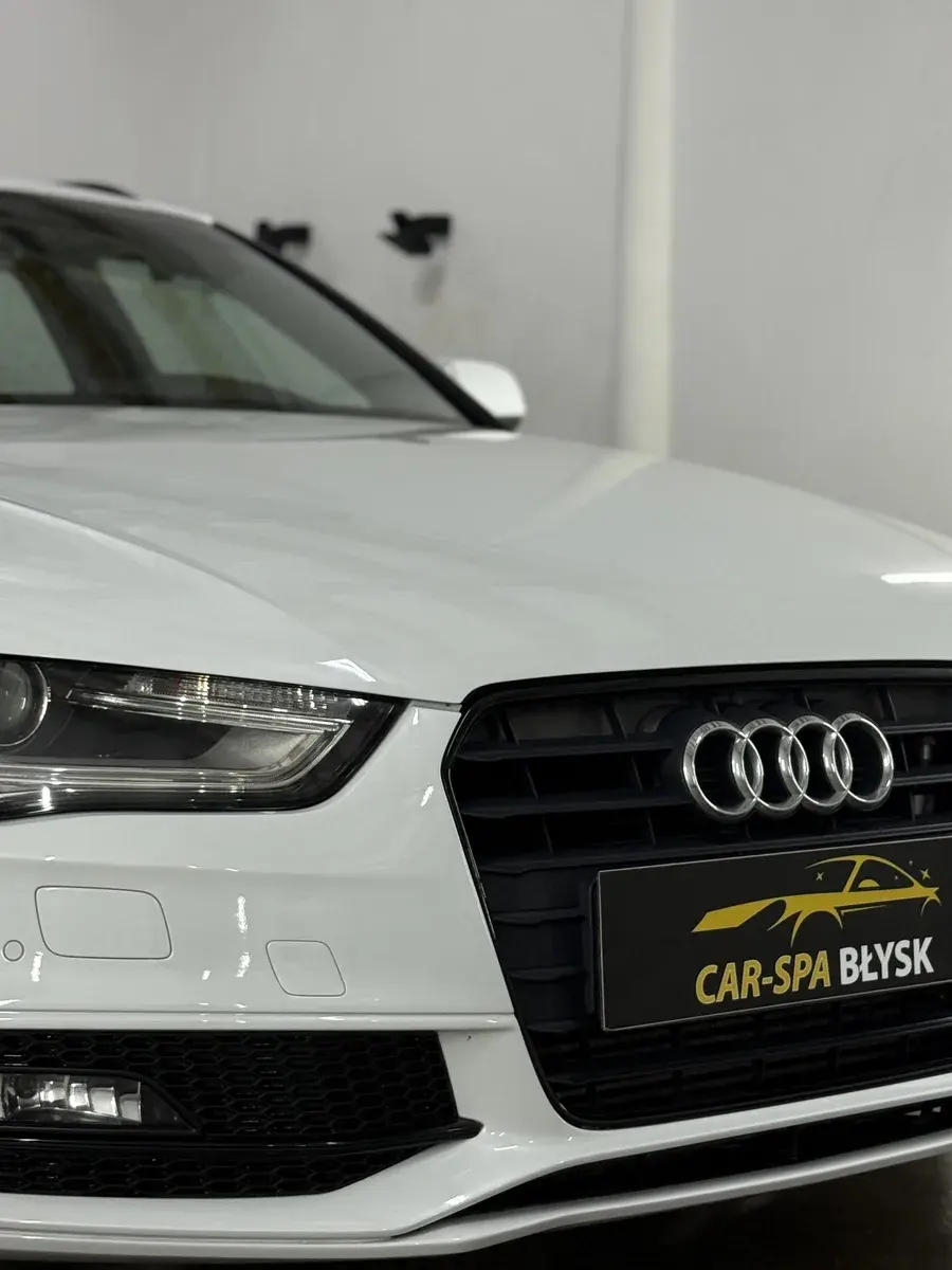 Zbliżenie na przód białego Audi A4 z plakietką Car-Spa Błysk
