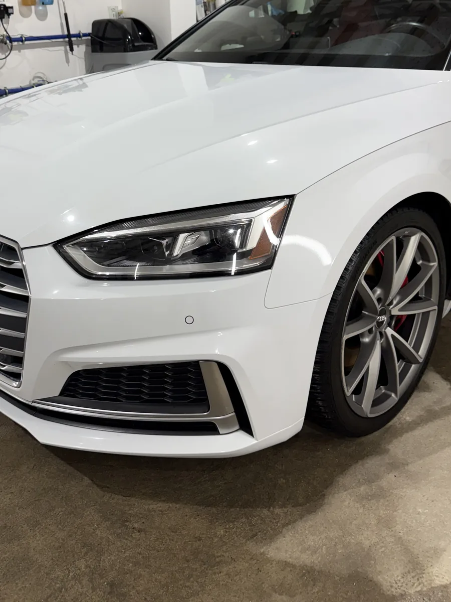 Przód białego Audi S5 w hali, zbliżenie na reflektor