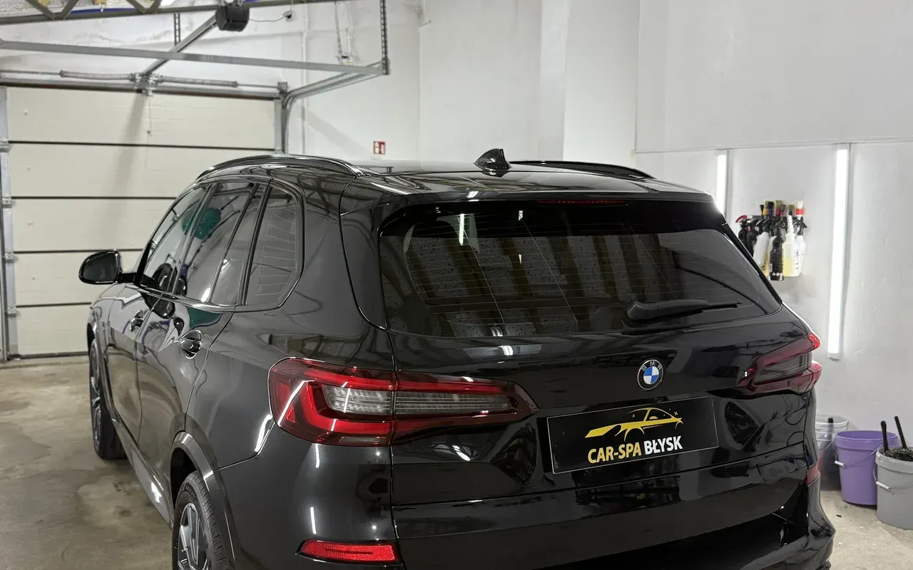 Tył czarnego BMW X5 w hali, w miejscu tablicy plakietka Car-Spa Błysk